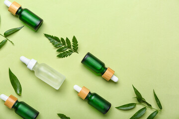 Bottles of cosmetic oil with plant twigs  on light green background