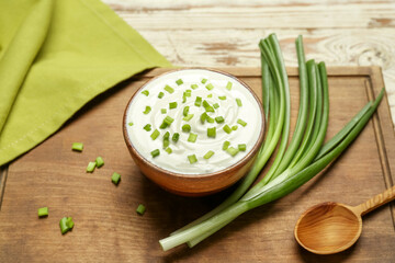 Bowl of tasty sour cream with green onion on table
