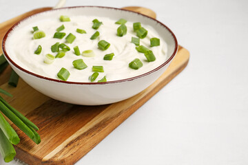 Bowl of tasty sour cream with green onion on light background