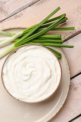 Fototapeta na wymiar Bowl of tasty sour cream with green onion on light wooden background