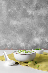 Bowl with sour cream and sliced green onion on white table near grunge wall