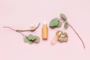Bottles with cosmetic oil and eucalyptus branch on pink background