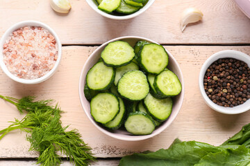 Bowls with pieces of fresh cucumber and spices on light wooden background