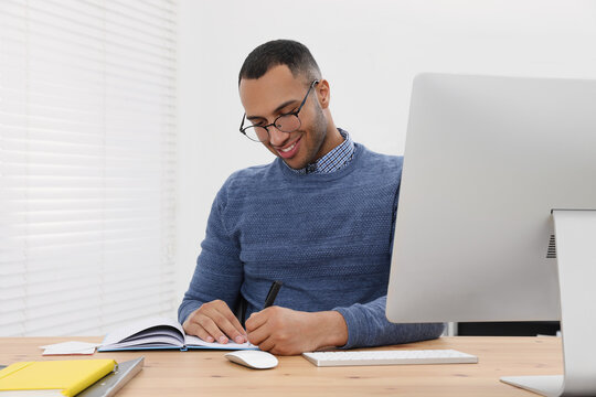 Happy young intern working at table in modern office