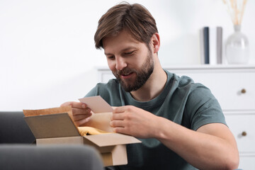 Happy man with greeting card near parcel at home. Internet shopping