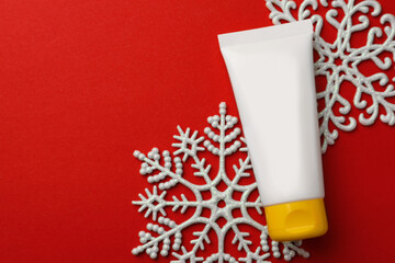 Tube of hand cream and snowflakes on red background, flat lay with space for text. Winter skin care