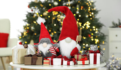 Fototapeta premium Funny Christmas gnomes and gift boxes on coffee table in room with festive decoration