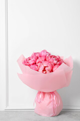 Bouquet of beautiful pink peonies on table near white wall