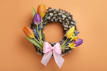 Willow wreath with different beautiful flowers and pink bow on orange background, top view © New Africa