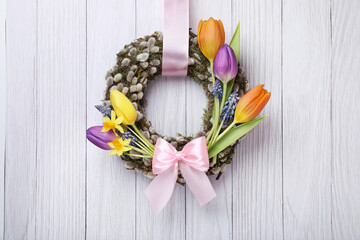 Willow wreath with different beautiful flowers and pink bow hanging on white wooden background © New Africa