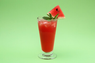 Glass of delicious drink with mint, ice cubes and cut fresh watermelon on light green background