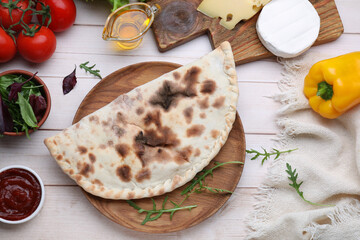 Delicious calzone and products on light wooden table, flat lay