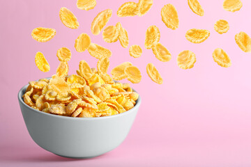 Tasty corn flakes falling into bowl on pink background