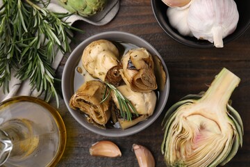 Bowl with delicious artichokes pickled in olive oil and ingredients on wooden table, flat lay