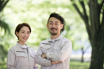 新緑の中、腕を組み見上げる作業着を着た作業員のイメージ コピースペースあり　カメラ目線