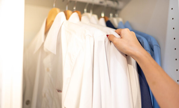 Female hand choosing clothes for checked pattern cotton polo shirt on the rack in cloth shop at a department store. Check price, discount, and promotion of clothing products.