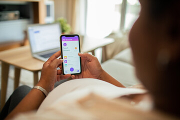 Young pregnant latina woman using a banking app on the couch in the living room