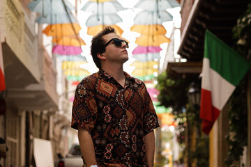 24 year old latino caucasian man with tattoos, traveling through the streets of cartagena enjoying colombia through the streets with umbrellas and the traditional and colorful buildings