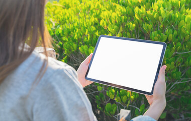 Woman sitting on a bridge in the garden and hand holding digital tablet mockup of blank screen, Take your screen to put on advertising.
