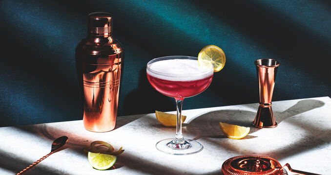 Pink lady classic cocktail drink with dry gin, grenadine syrup, lemon juice and egg white, dark green background, bright hard light, shadow pattern. Banner
