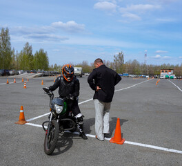 A young woman is learning to ride a motorbike in a motorcycle school. She is taught by a teacher.