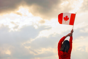 Woman Waving Canadian Flag Looking at the Sky. Optimistic girl holding national flag celebrating...