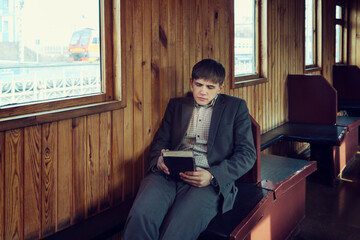 young man in a vintage railway car is sitting reading a book and looking out the window