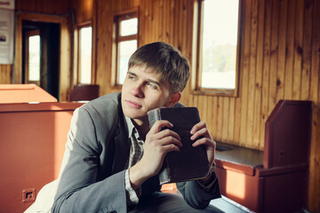 young man in a vintage railway car is sitting reading a book and looking out the window