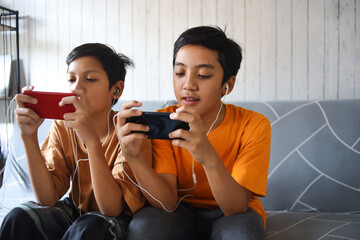 Two kids playing games with gadgets on couch. Modern communication and gadget addiction concept.