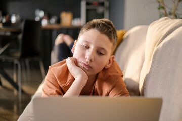 Teen boy study or play game on laptop home interior background. Guy doing homework and typing on laptop