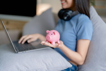 Asian young woman holding a piggy bank and using computer, Savings concepts.