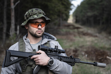 Fototapeta premium A soldier in goggles and a panama hat on his head with a rifle with an optical sight in his hands.