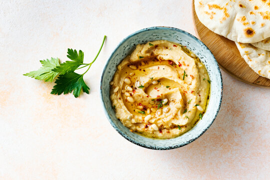 Homemade hummus with pine nuts and pita on a beige background, top view.