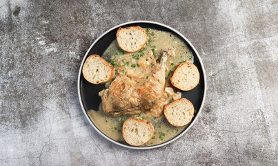 Stewed chicken leg with garlic and bread  on a round plate on a dark grey background. Top view, flat lay