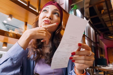 The girl's face was etched with a mix of confusion as she scrutinized the bill in front of her in...