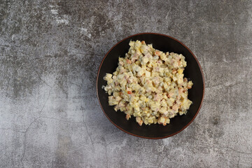 Homemade Russian salad or Olivier from boiled vegetables and sausage in a bowl on a dark background. Top view, flat lay  .