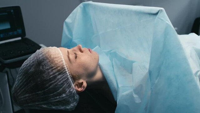 Medium shot of young Caucasian female patient lying with eyes closed on surgical table in operating theater