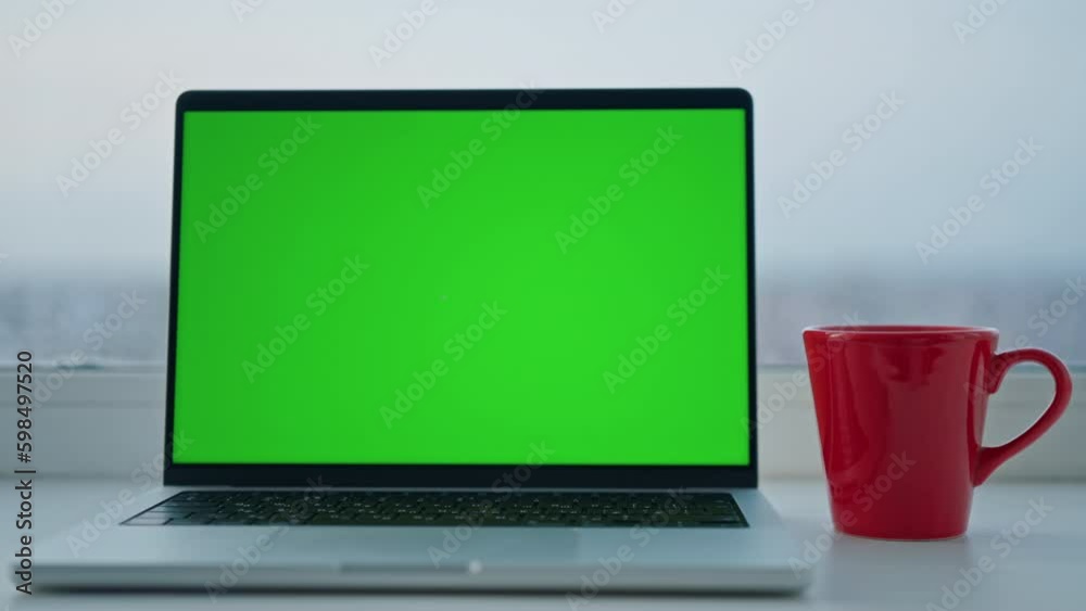 Poster laptop with green isolated screen red cup on the desk in front of big window home office in winter s