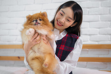 Beautiful asian woman holding and looking furry dog with smile on bedroom.