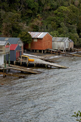 Colourful row of boathouses and boat ramps in a sheltered bay surrounded by bush-covered hills, Stewart Island, New Zealand.