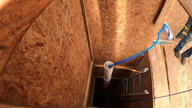 Man pass wood brace to another man working on the bottom of the hole. Wide angle view of the home made water well being dug next to mobile house.