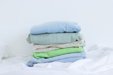 Pile of clothes on white, pastel color palette of stacked sweaters and jeans, fresh clothing folded for ironing