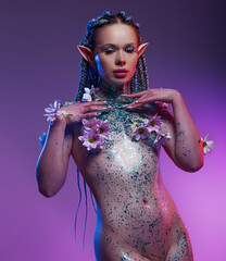 A charming female elf. One with nature and organically purity. The nude model her body covered flowers and sparkle glitter on a violet background