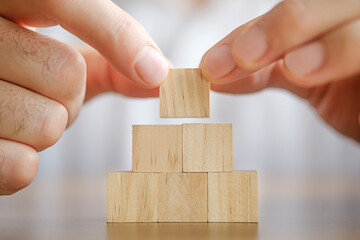 Close-up photo of putting wooden block on top of pyramid. Planning business growth. Horizontal concept with copy space for your text.