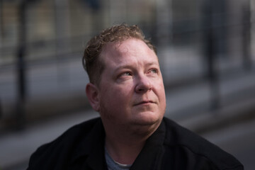 Obraz premium A disabled transman rides his powerchair in the city. His intimate portrait is accentuated by dramatic afternoon light to express strength, and the humanity of accessibility and gender rights.