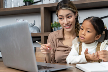 Beautiful mother teaching her lovely daughter to do homework in living room