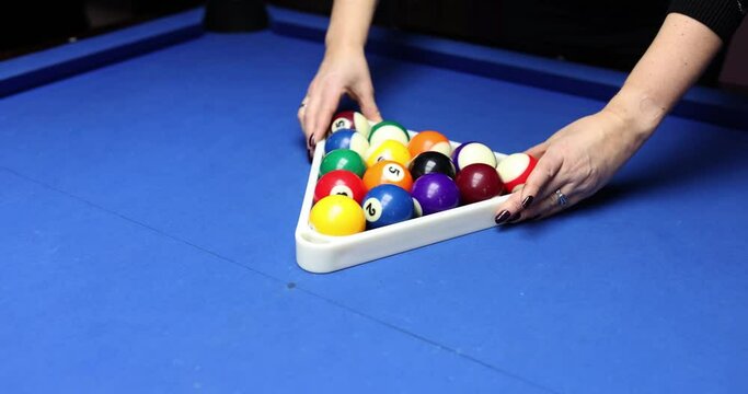 Female hands arrange billiard balls in form of equilateral triangle. Woman with black manicure uses triangular frame before new billiard game