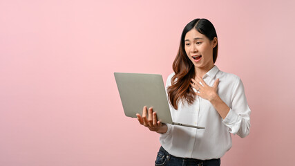 Adorable young Asian woman feeling surprised while looking at laptop, isolated background.