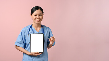 Happy doctor showing blank screen tablet to the camera while standing on pink isolated background.