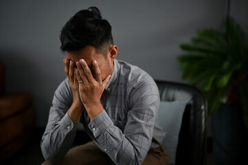 Stressed and depressed Asian man is covering his face, crying about his failures in life